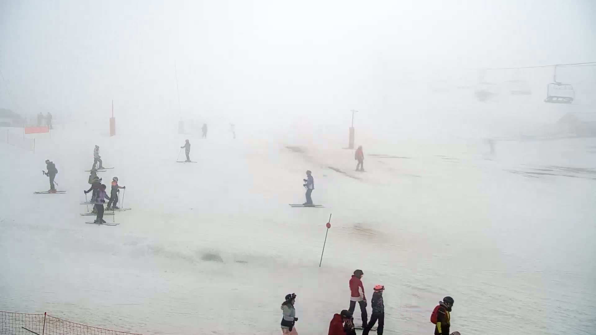 Several skiers are scattered across a snow-covered ski slope shrouded in dense fog.