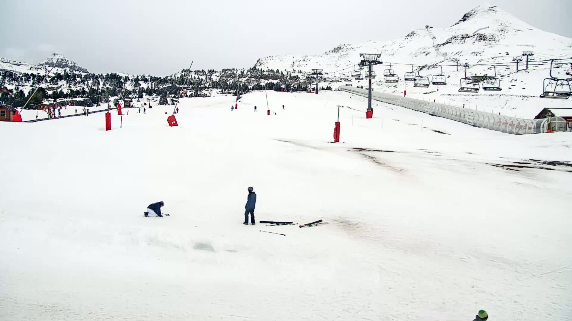A snowy ski slope with a chairlift and several skiers, under an overcast sky.