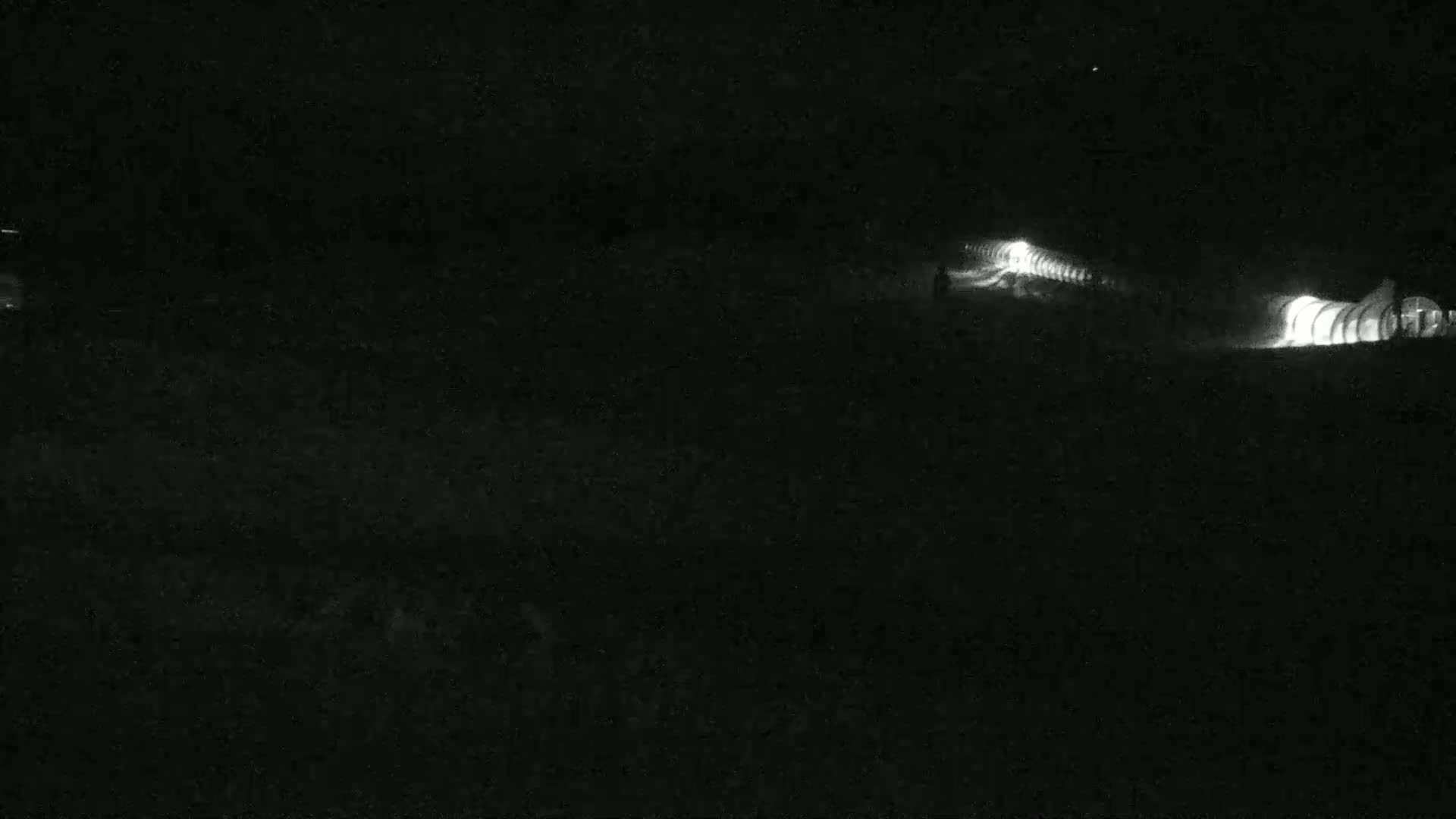 Two illuminated structures are visible at night in a dark, possibly snowy or icy landscape.