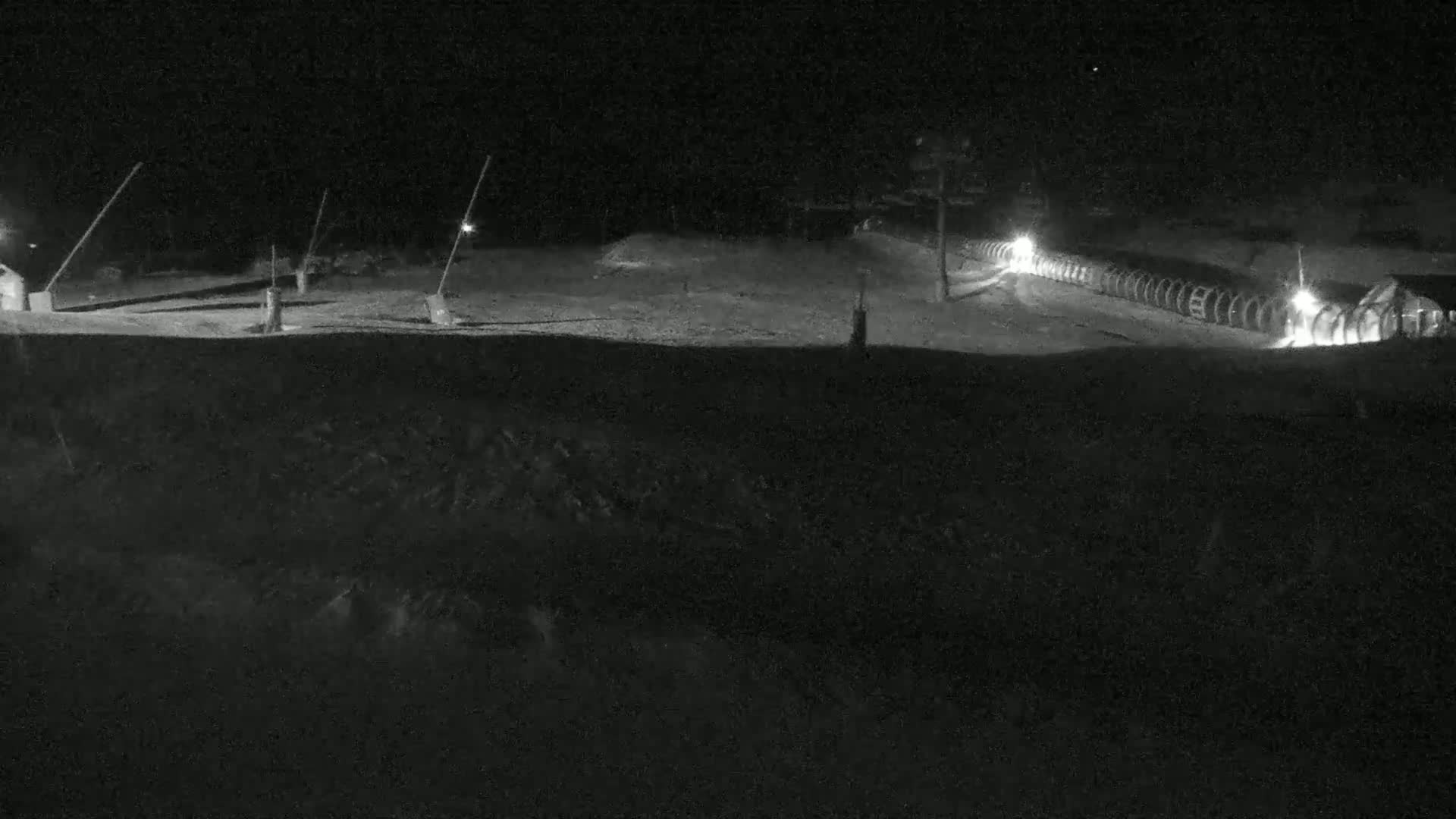 A nighttime, snow-covered area with a line of illuminated objects, possibly snowmaking equipment, extending from left to right.