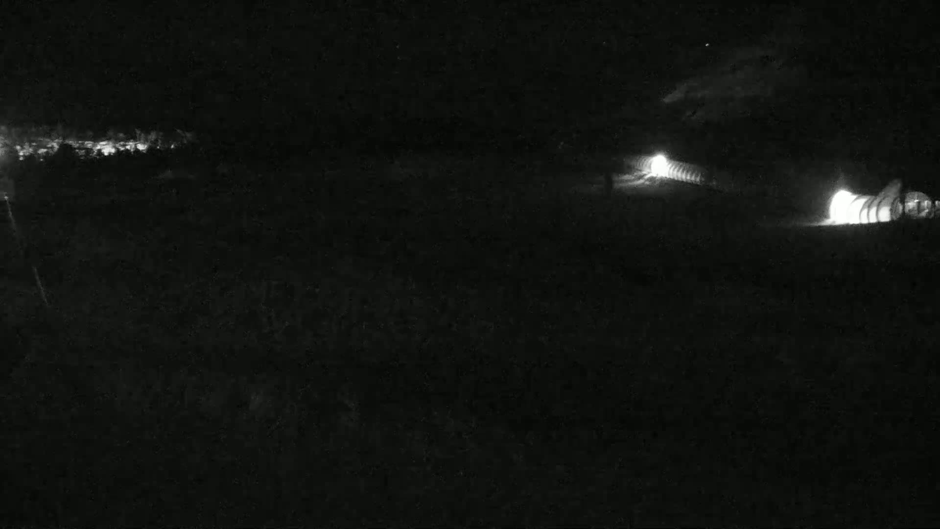 At night, two illuminated structures are visible in the distance, with a faint light source in the upper left corner.