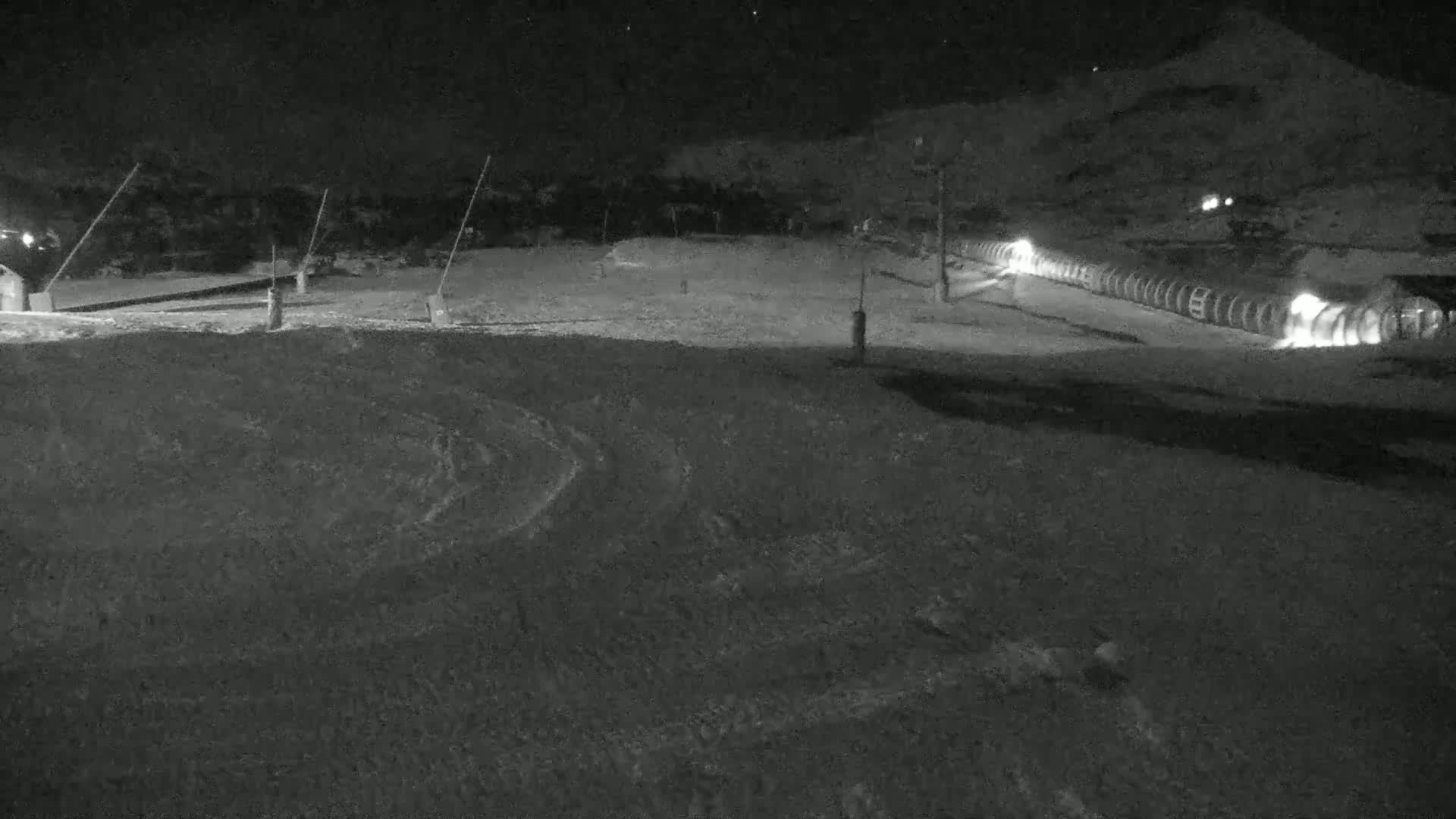 A snow-covered ski slope at night, illuminated by lights along a ski lift.