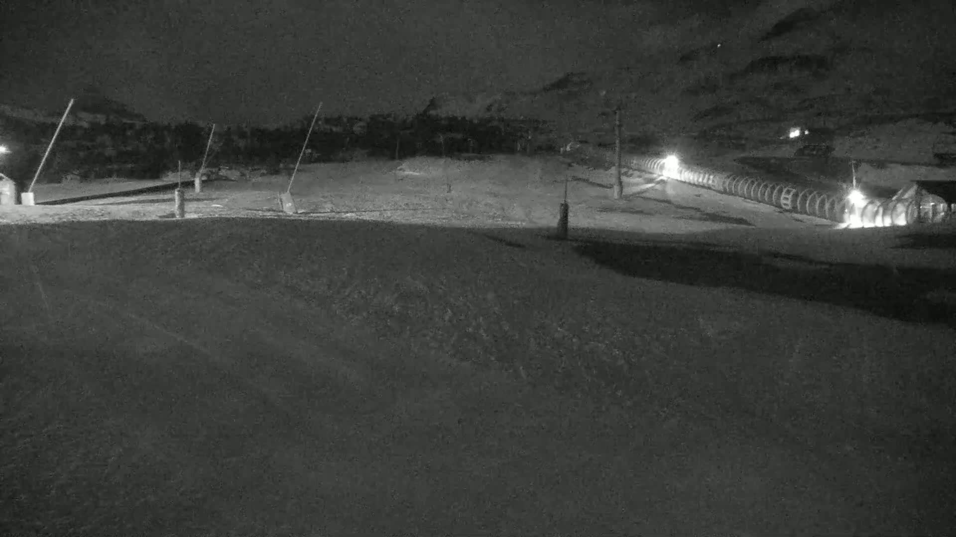 A snow-covered slope at night, illuminated by lights near a ski lift.