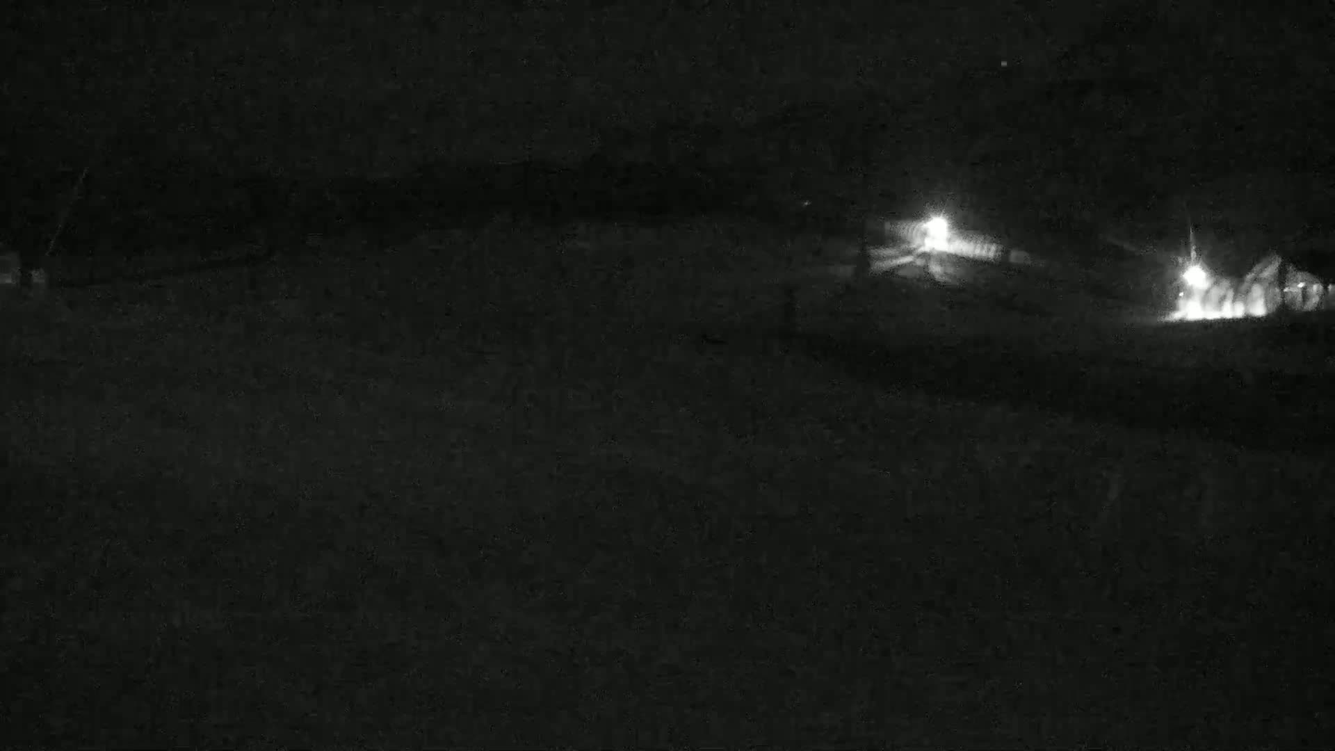 A nighttime, low-light view of a dark, snow-covered landscape with faintly visible structures and lights in the distance.