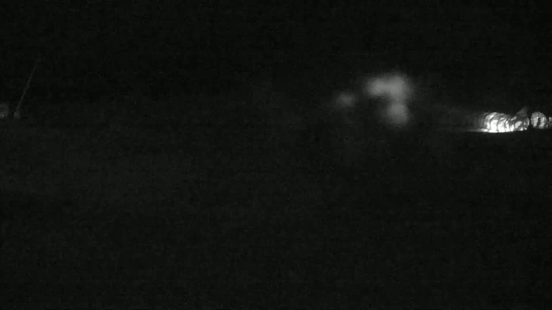 A nighttime, low-light image shows a blurry line of bright lights in the distance, likely vehicles, on a dark, flat surface.