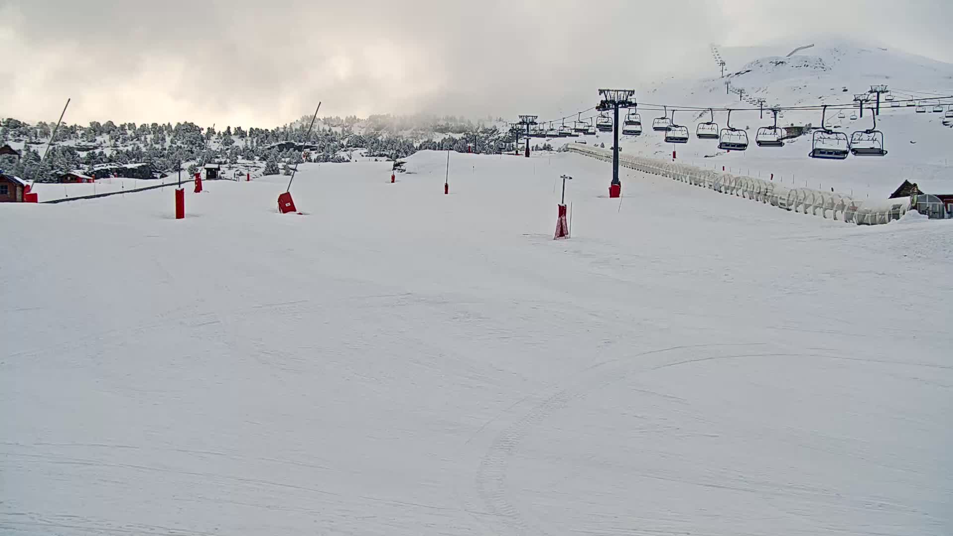 A snow-covered ski slope with a chairlift and a few red markers under an overcast sky.
