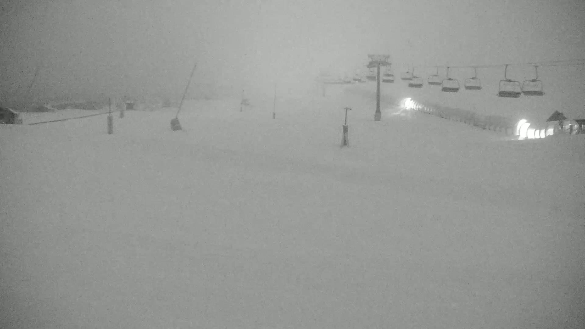 A snow-covered ski slope with a chairlift in the background during a heavy snowstorm.