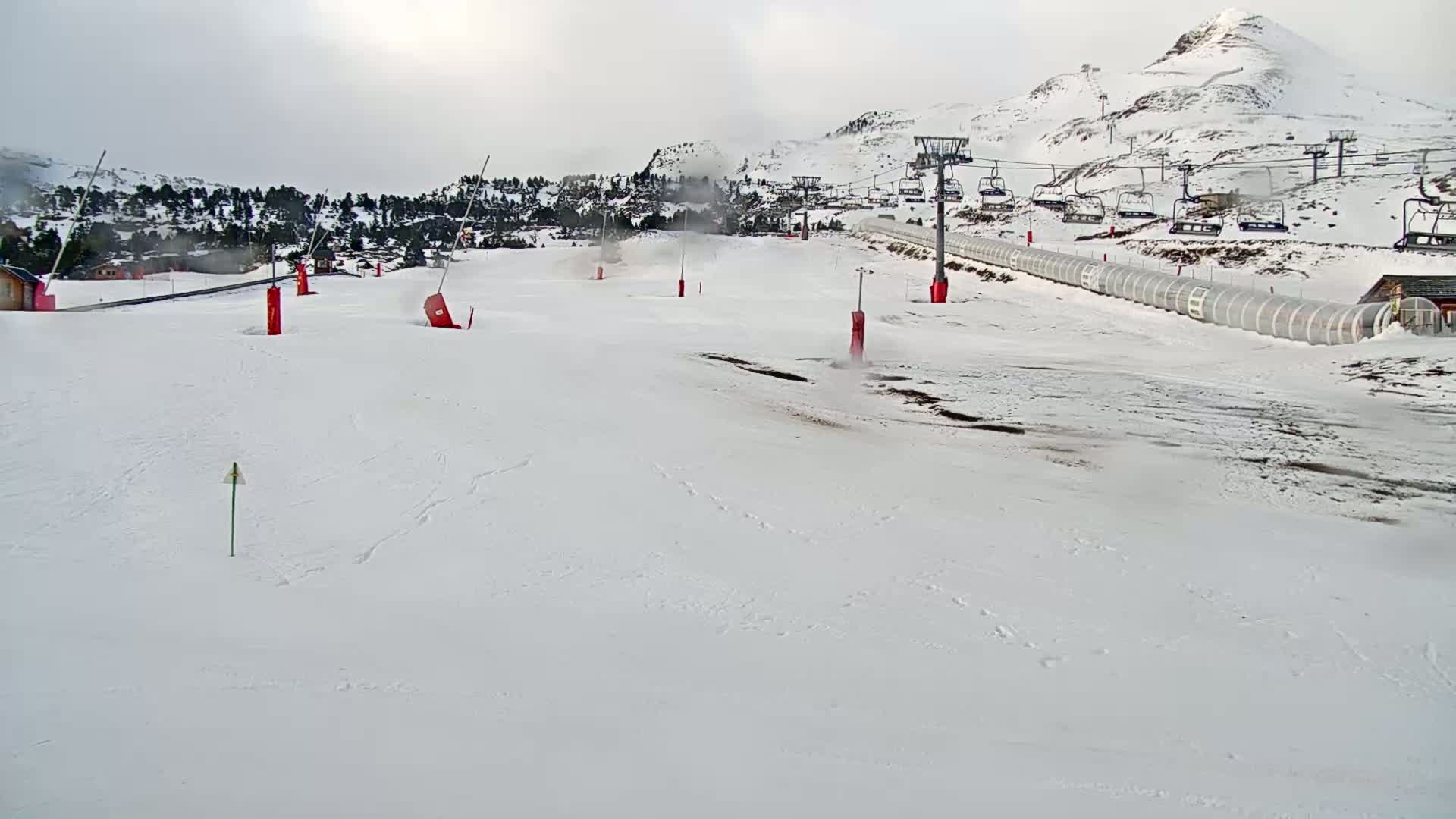 A snow-covered ski slope with several chairlifts and red markers is visible under an overcast sky.