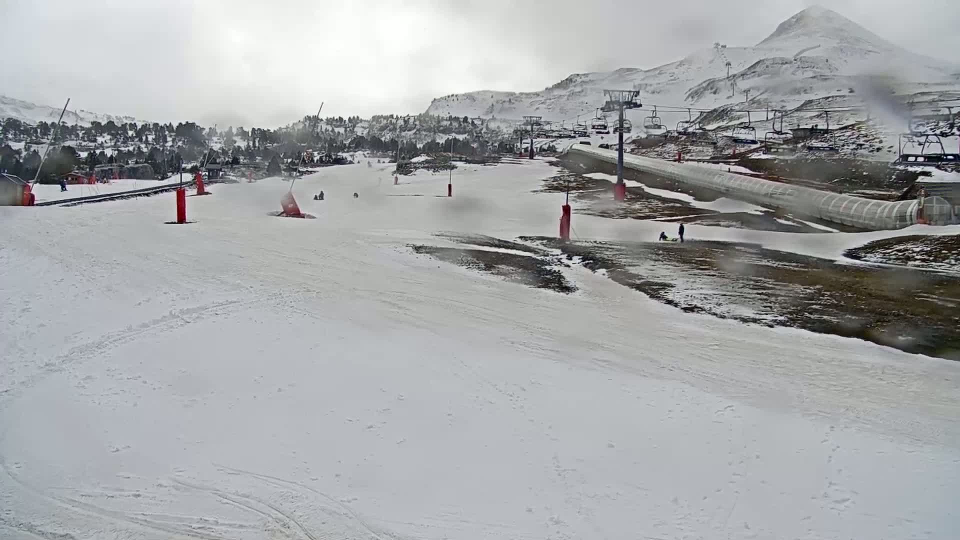 A snowy ski slope with several chairlifts and a few people visible on an overcast day.
