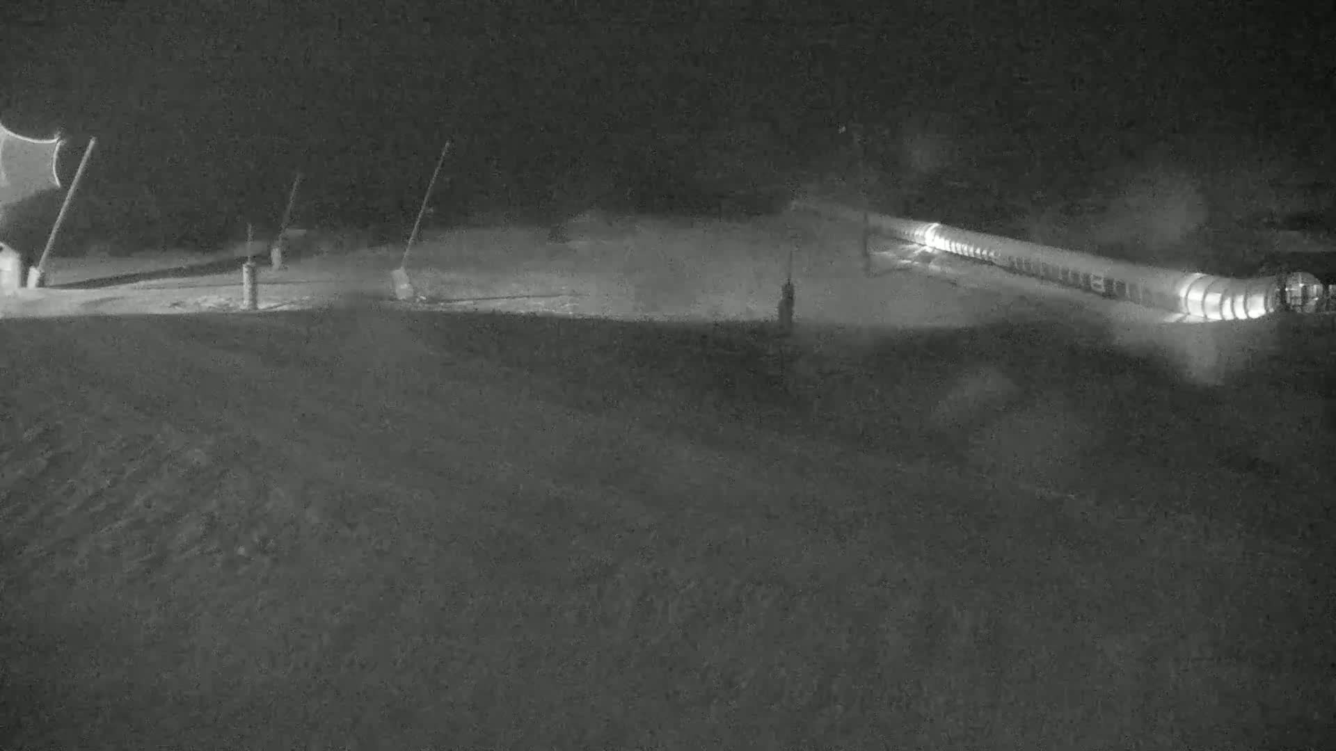 A long, illuminated structure is visible on a snow-covered ground at night.