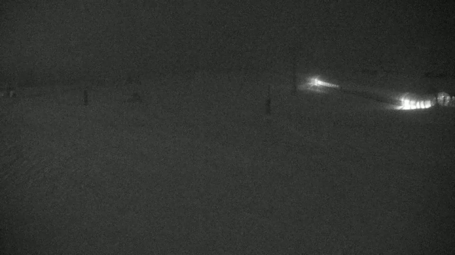 At night, faint lights from vehicles are visible on a dark, snow-covered surface.