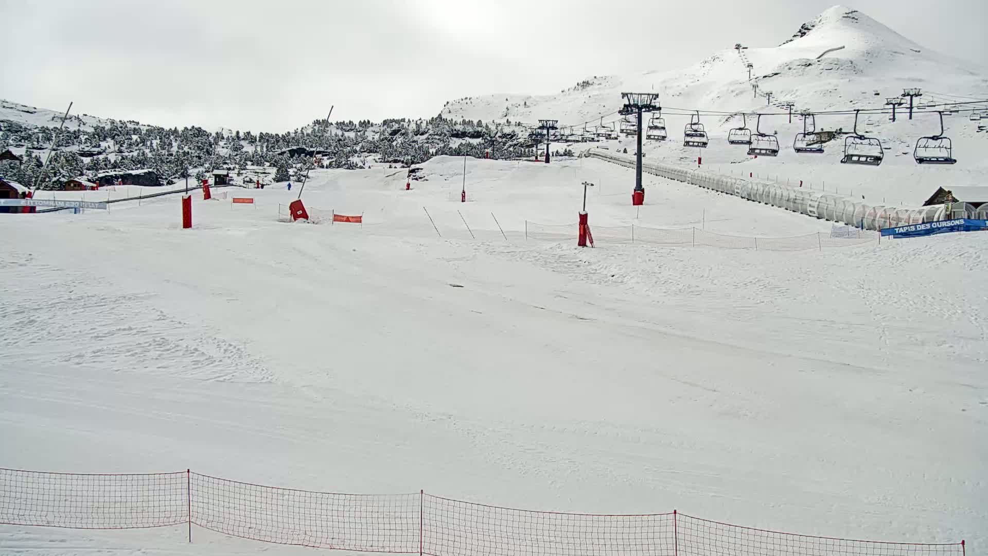 A snow-covered ski slope with a chairlift and a few skiers, under an overcast sky.
