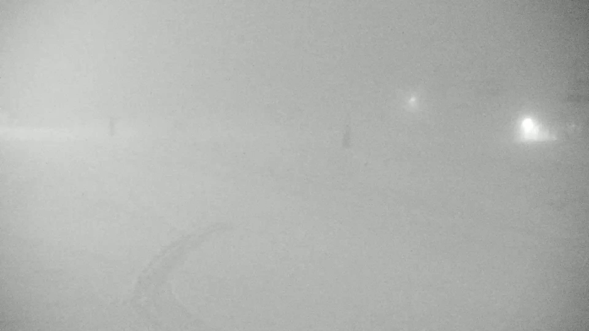 A heavily fogged or snowy outdoor scene shows faint lights in the distance.