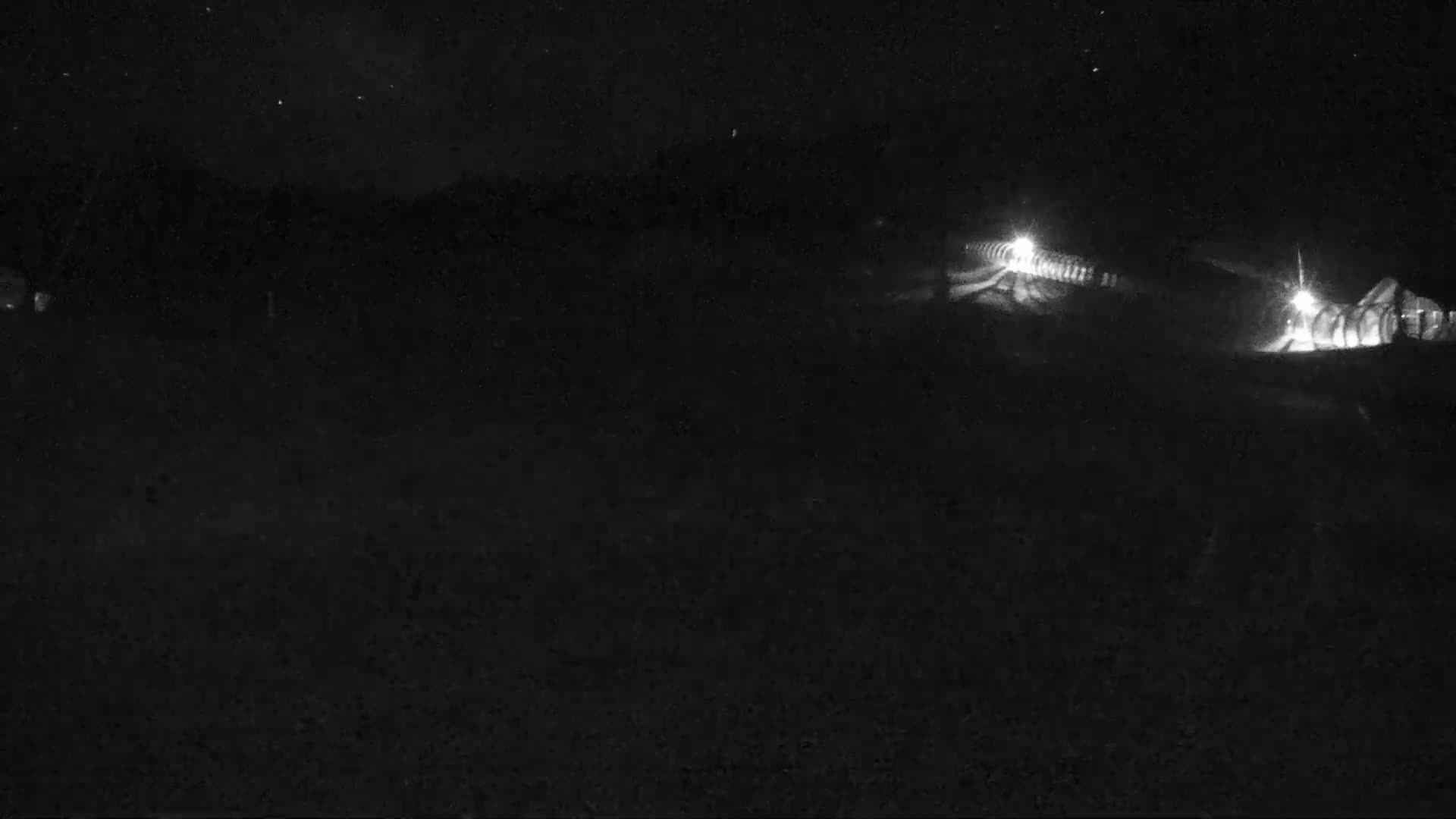 A nighttime, low-light view of a dark landscape with faintly visible structures and lights in the distance under a starry sky.