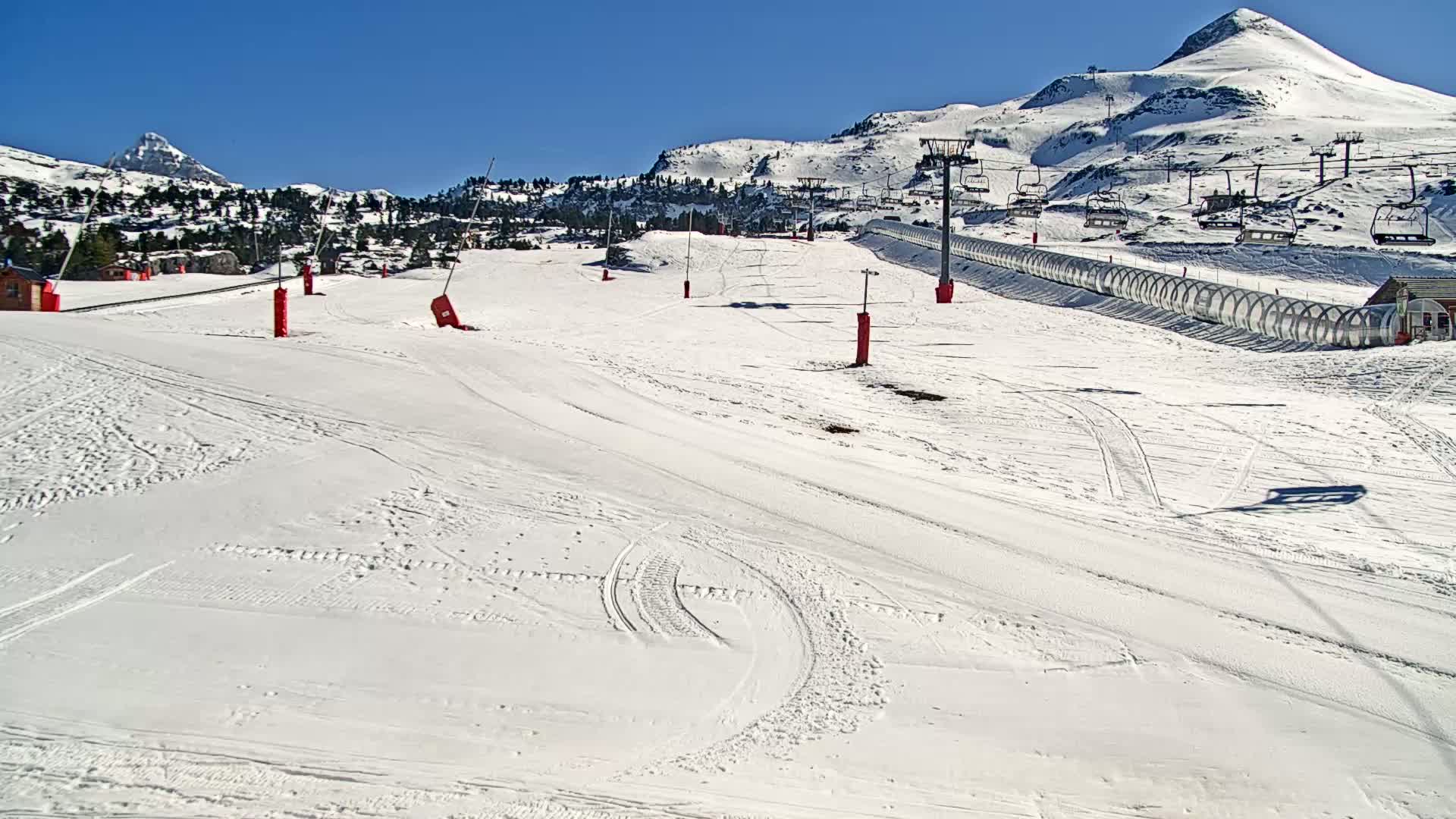 A snow-covered ski slope with ski lifts and a clear, sunny sky.