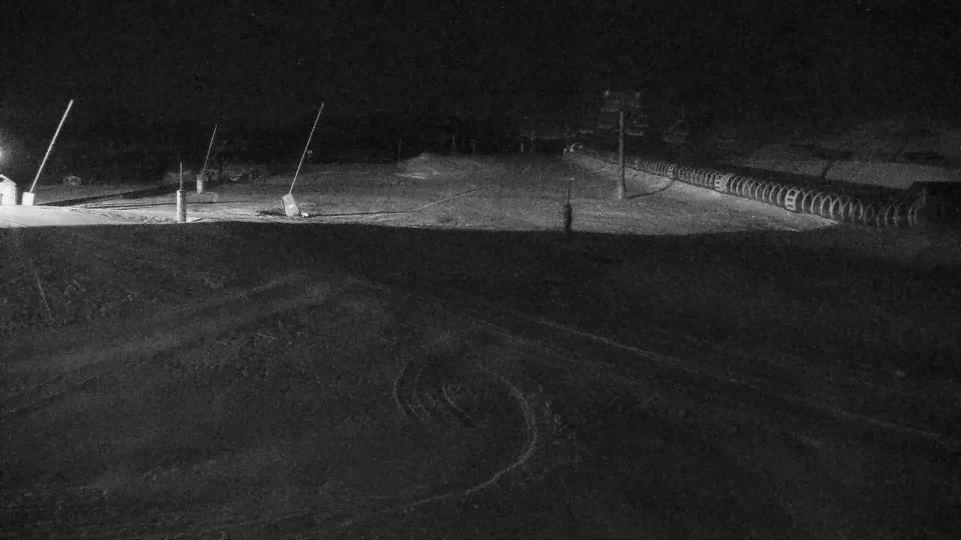 A snow-covered ski slope is illuminated at night by artificial lights.