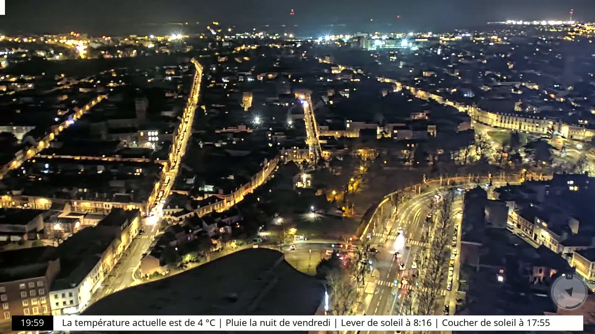 A nighttime aerial view of a city with illuminated streets and buildings, under rainy conditions.