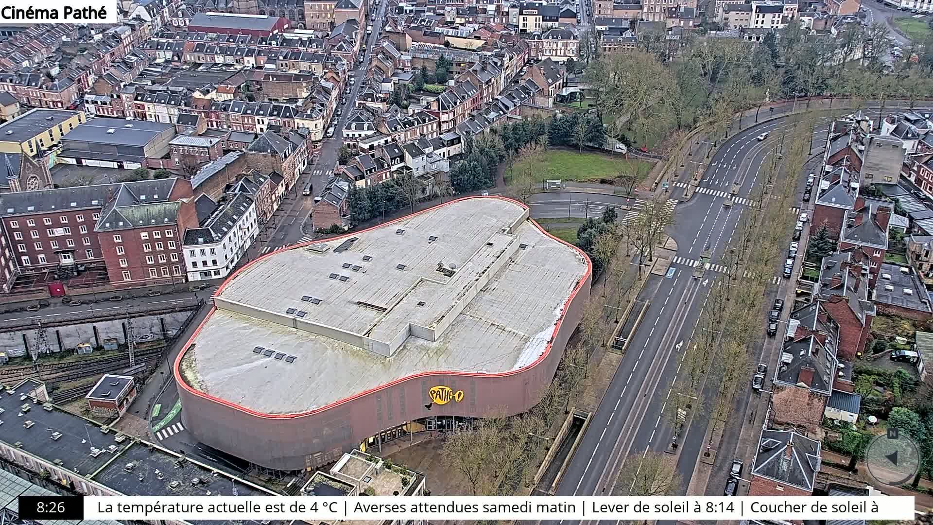 An aerial view of a city street and a large building with a curved roof, on a cloudy day.