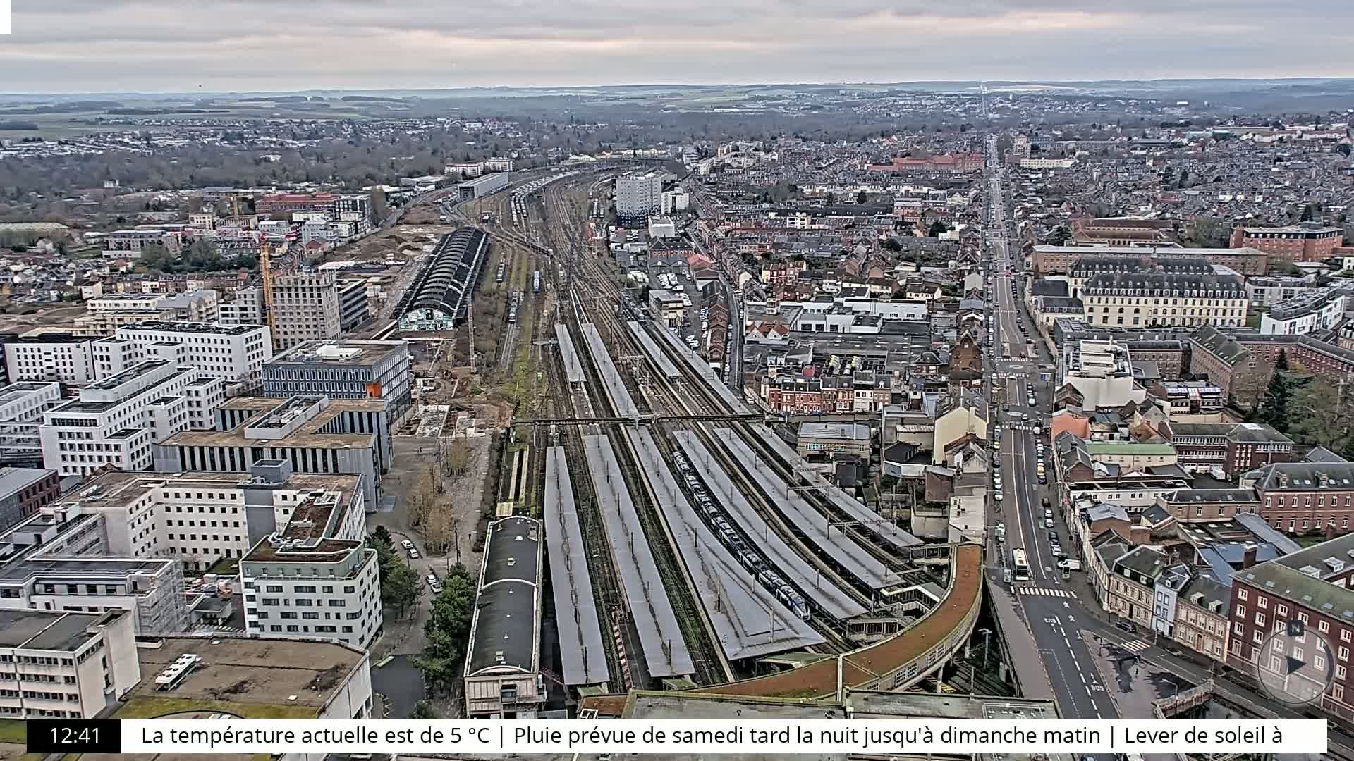 A high-angle, long shot of a city with a large train station, under an overcast sky.