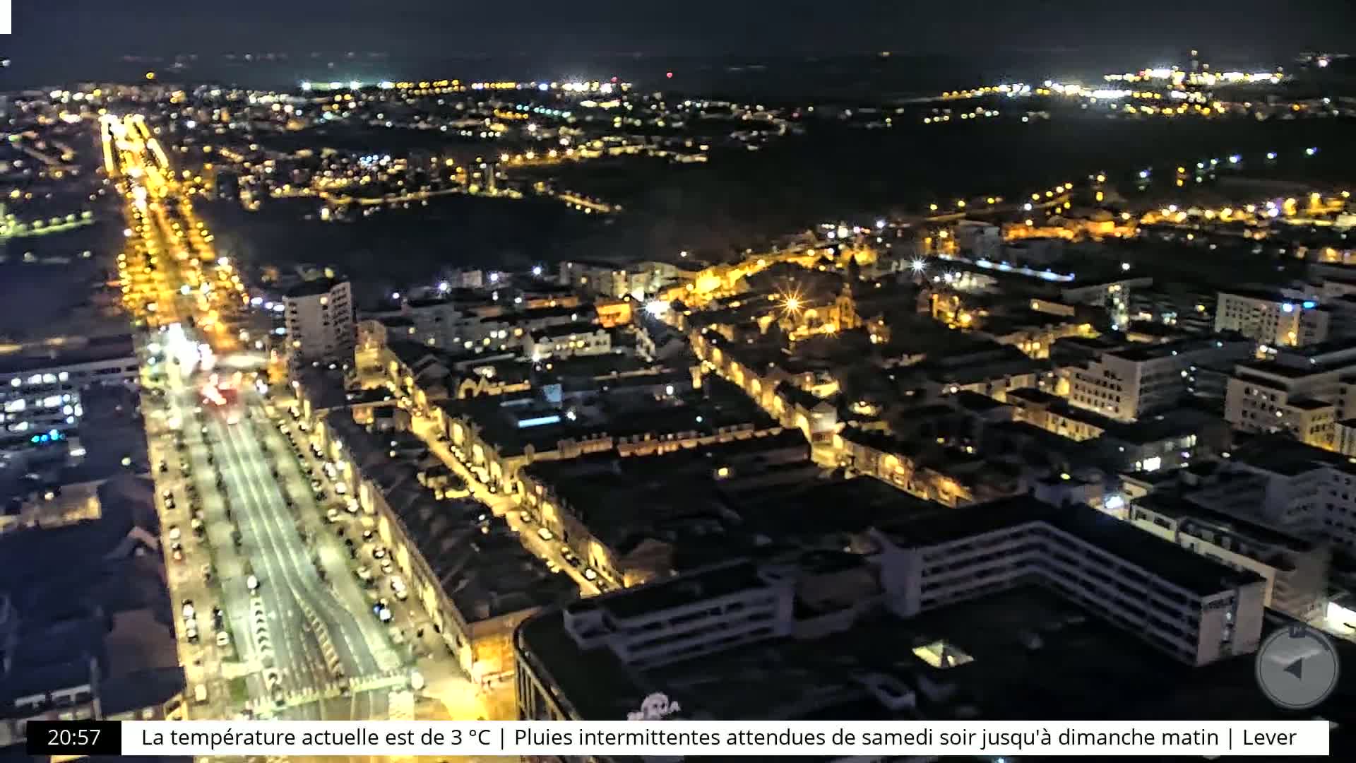 An aerial nighttime view of a city with brightly lit streets and buildings, under a dark sky.