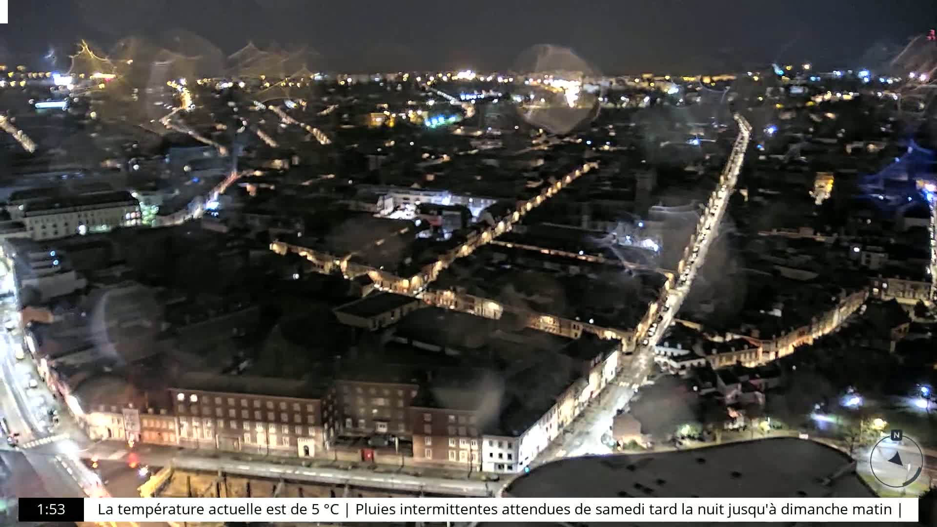 A nighttime aerial view of a city with illuminated streets and buildings, under a slightly hazy sky.