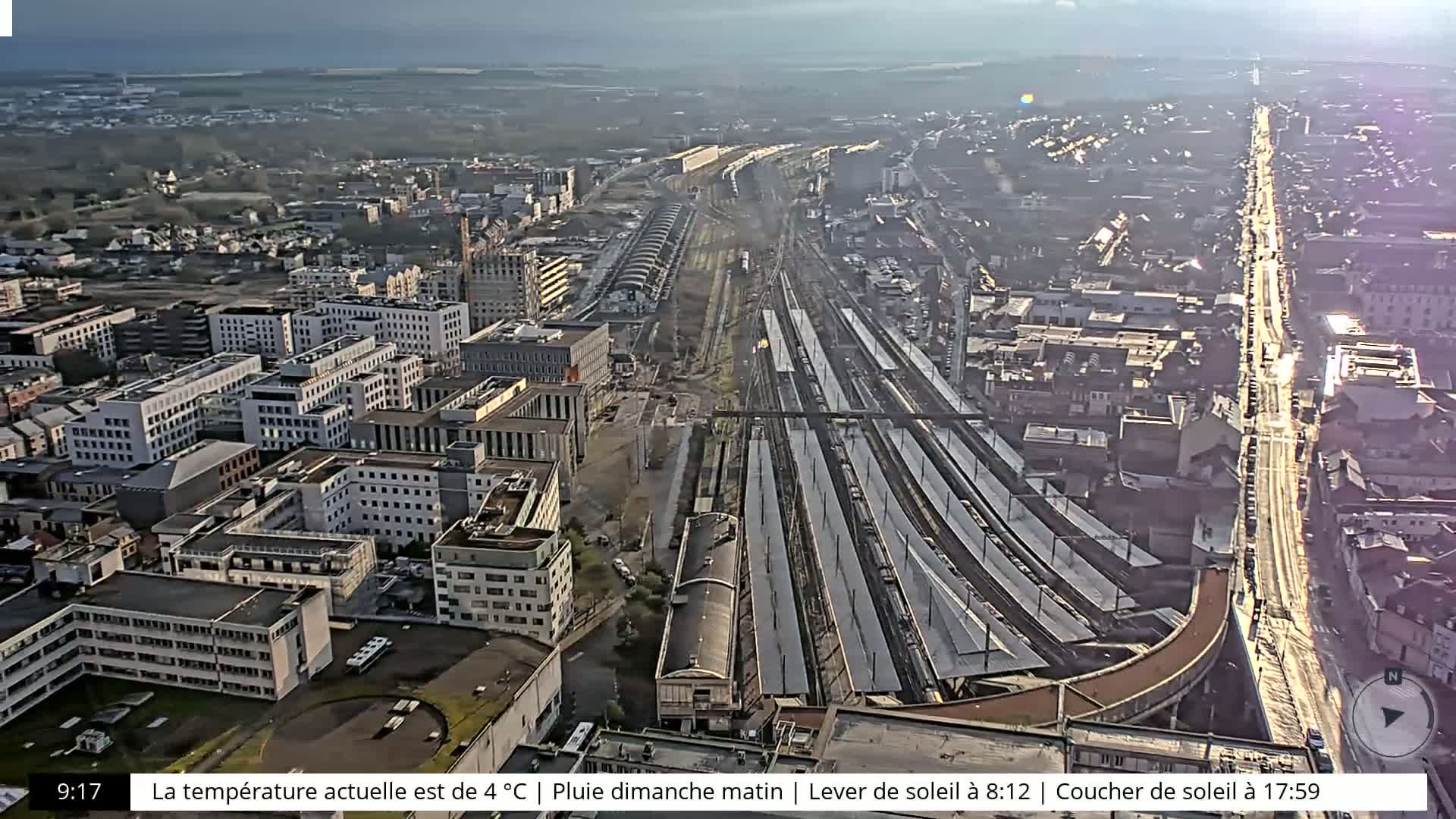An aerial view of a city with a large train station, under an overcast sky.