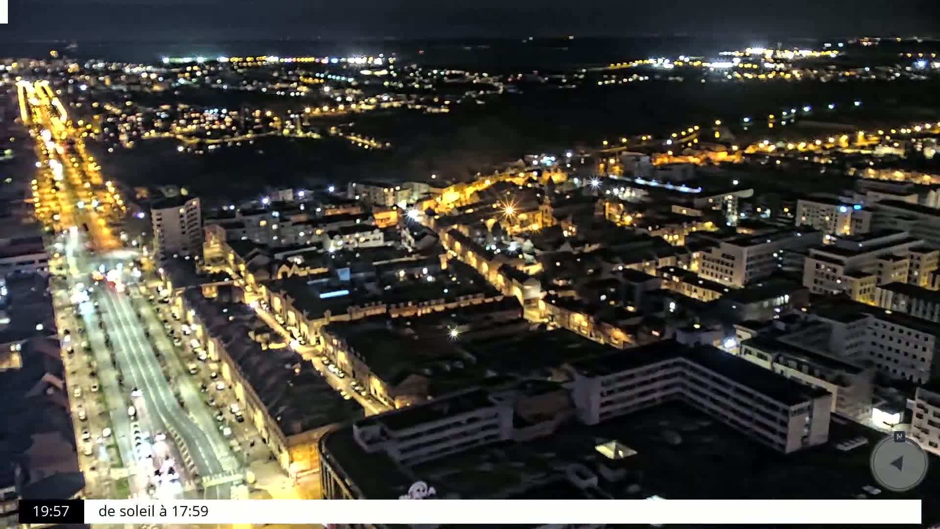 A nighttime aerial view shows a city with brightly lit streets and buildings.