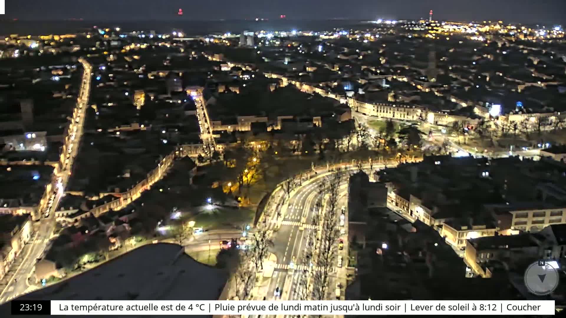 A nighttime aerial view of a city with illuminated streets and buildings, showing a dark, possibly overcast sky.