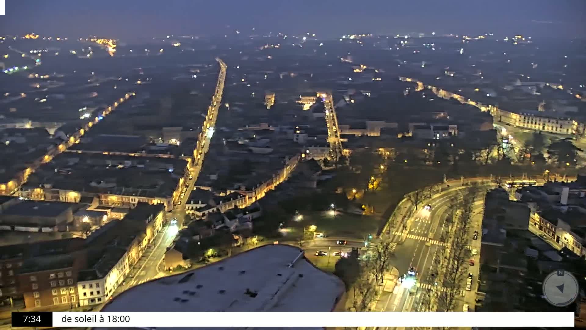 A nighttime, high-angle view of a city with illuminated streets and buildings, under a hazy sky.