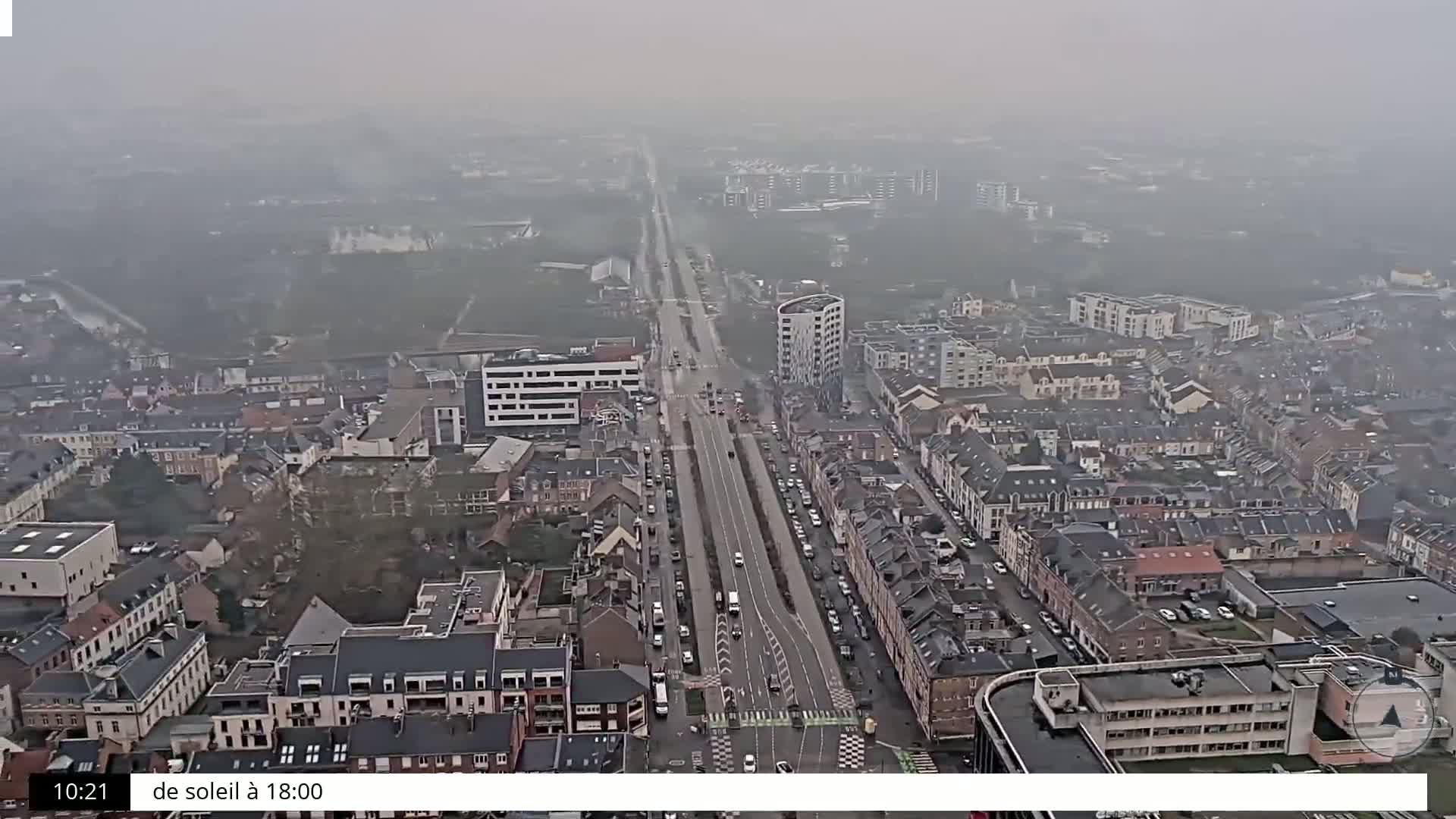 An aerial view shows a city with a long road running through it on an overcast day.
