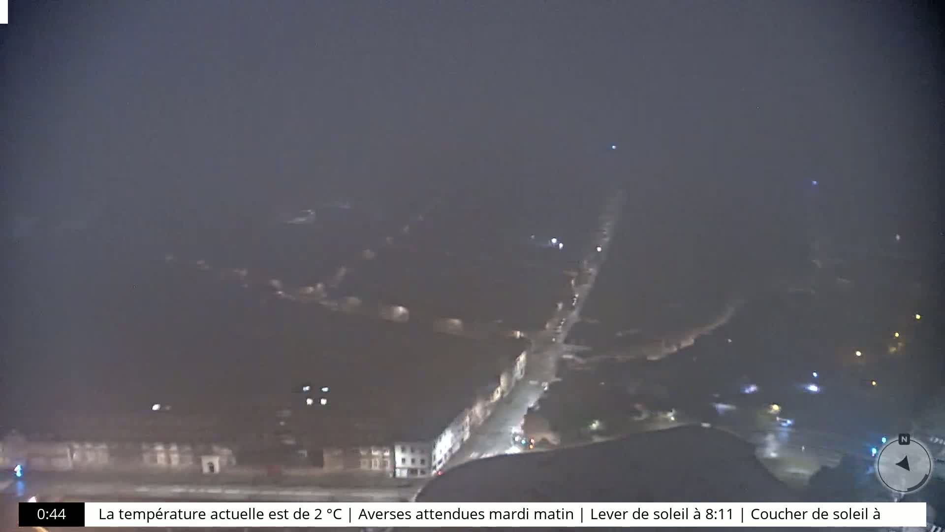 A nighttime, high-angle view of a town under a hazy, dark sky with some faint lights visible.