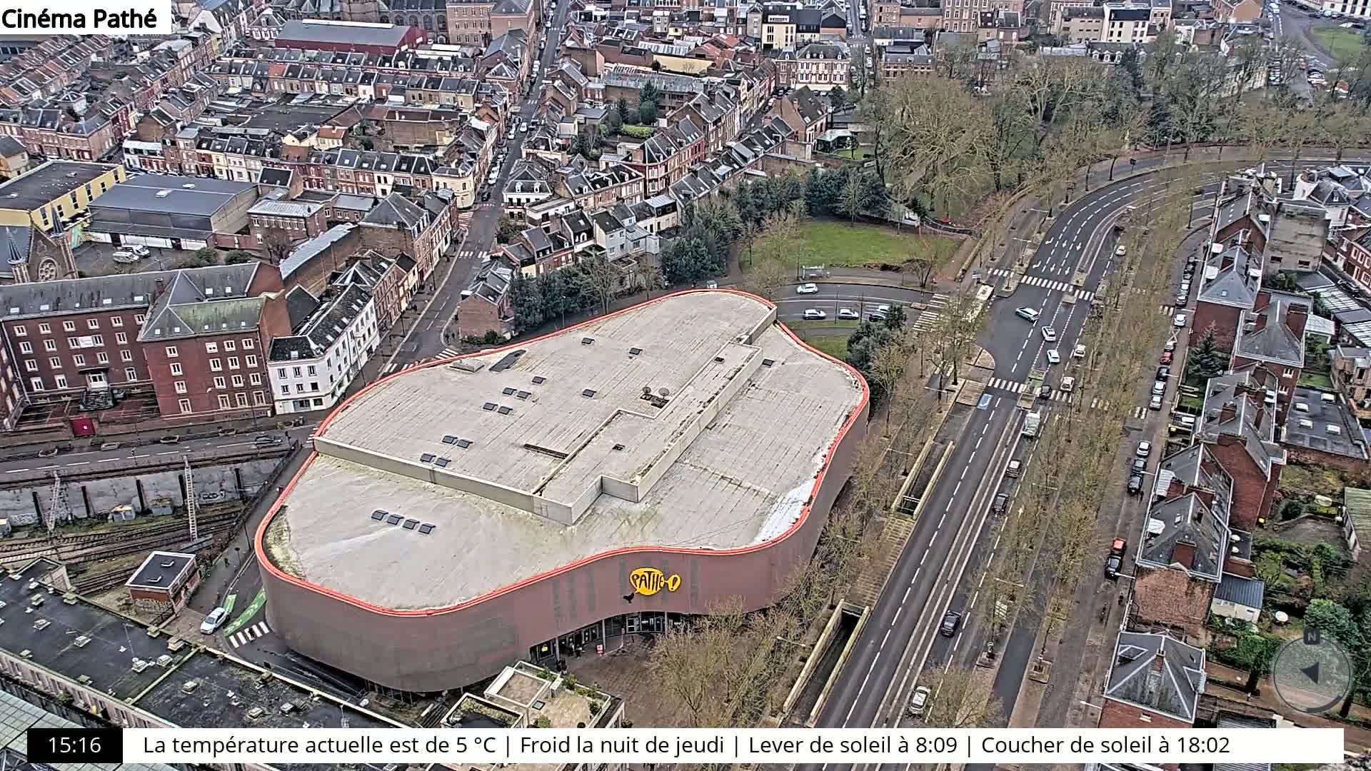 An aerial view of a city on an overcast day shows a curved-roof building, roads, and residential areas.