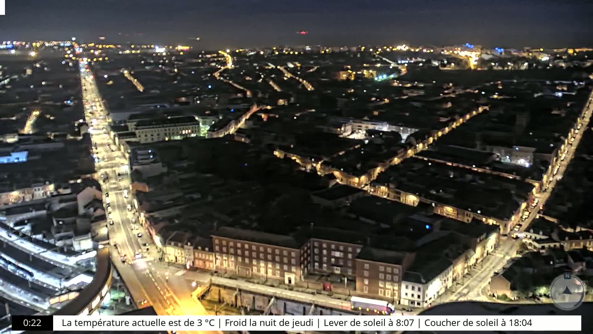 A nighttime aerial view of a city with brightly lit streets and buildings, under a clear, cold sky.