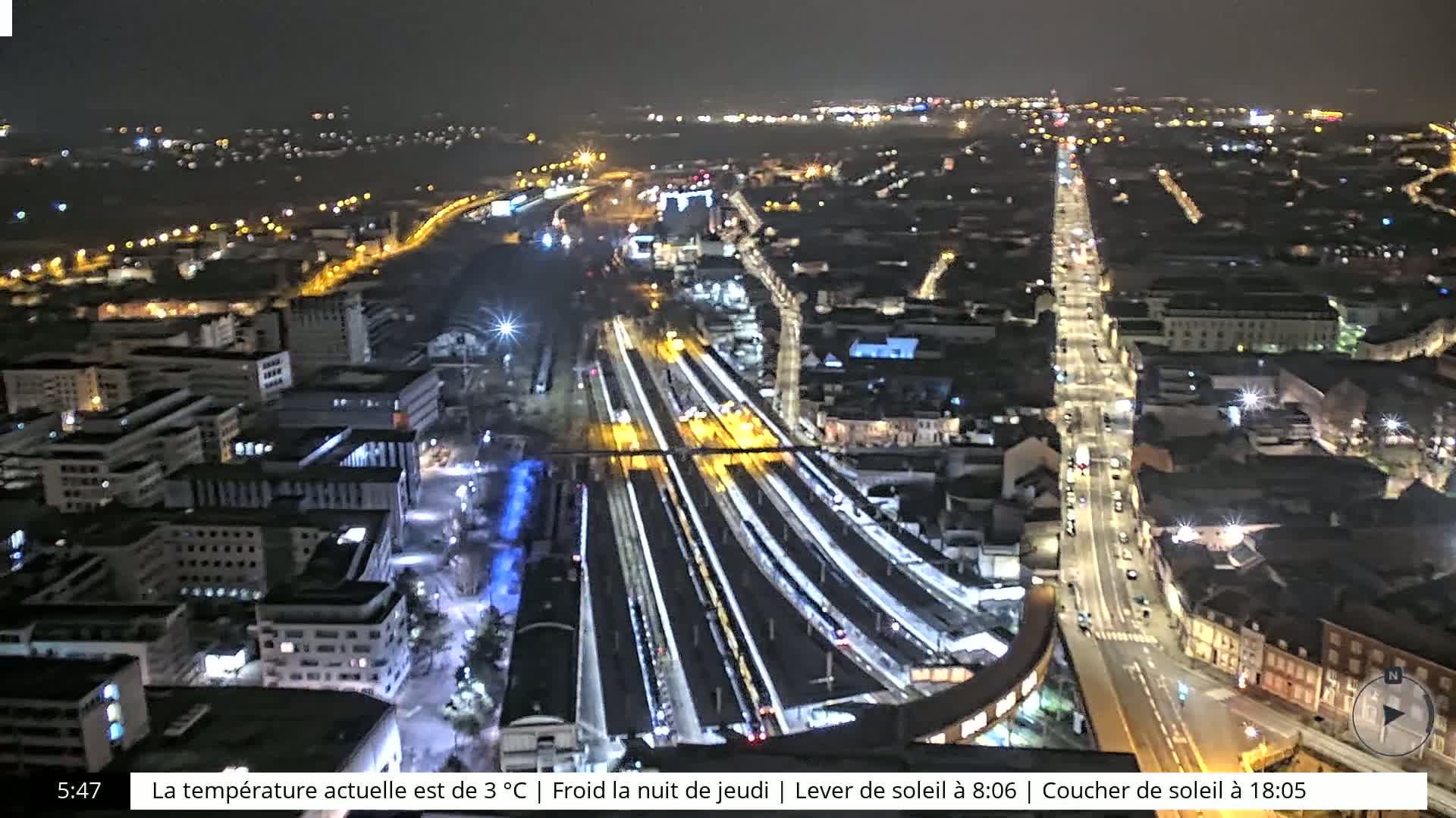 A nighttime aerial view of a city's train station and surrounding streets, illuminated by streetlights.