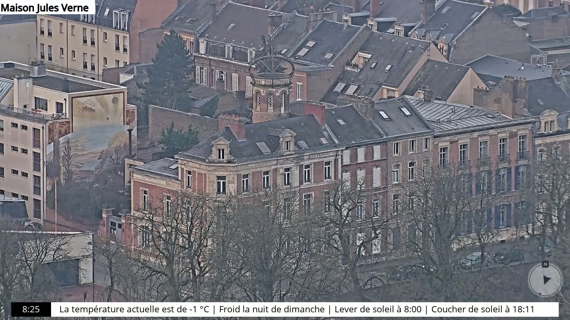 An aerial view of a city block with several multi-story buildings, a mural, and bare trees on a cold Sunday night.