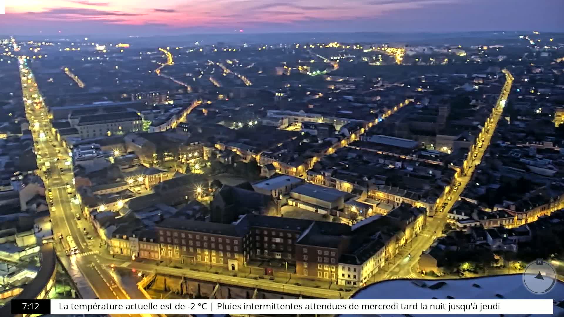 An aerial, nighttime view of a city with illuminated streets and buildings under a twilight sky.