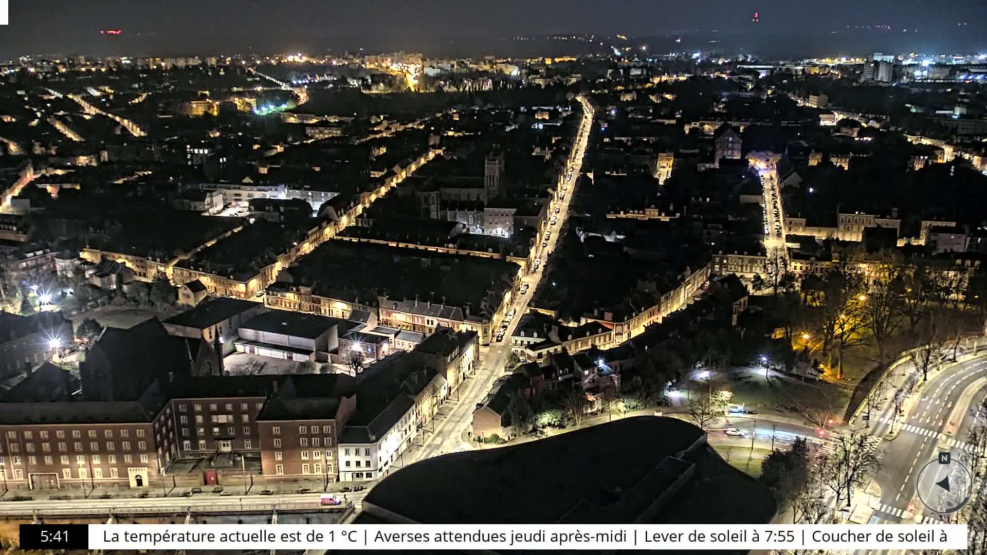 A nighttime aerial view of a city with a long, brightly lit street running through its center, under a clear sky.