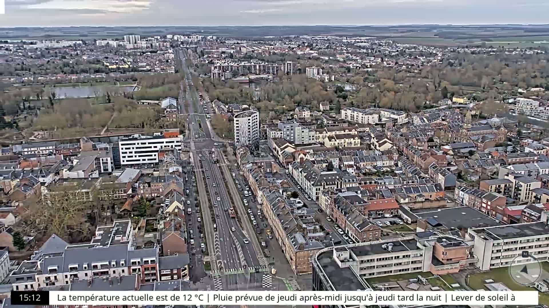 An aerial view of a city on an overcast day shows a long, multi-lane road cutting through a densely packed residential area.