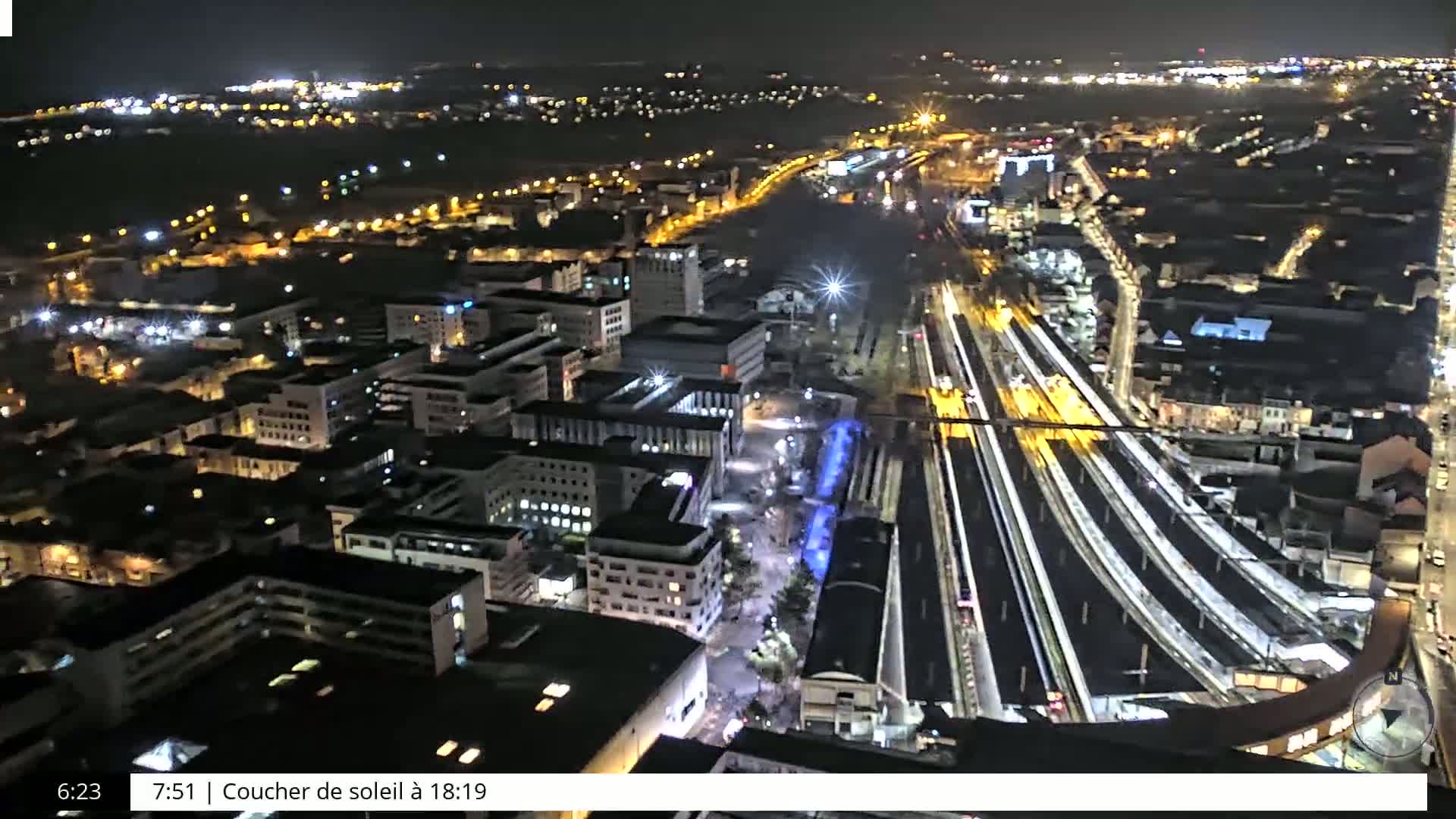 A nighttime aerial view of a brightly lit city with a train station and surrounding buildings.