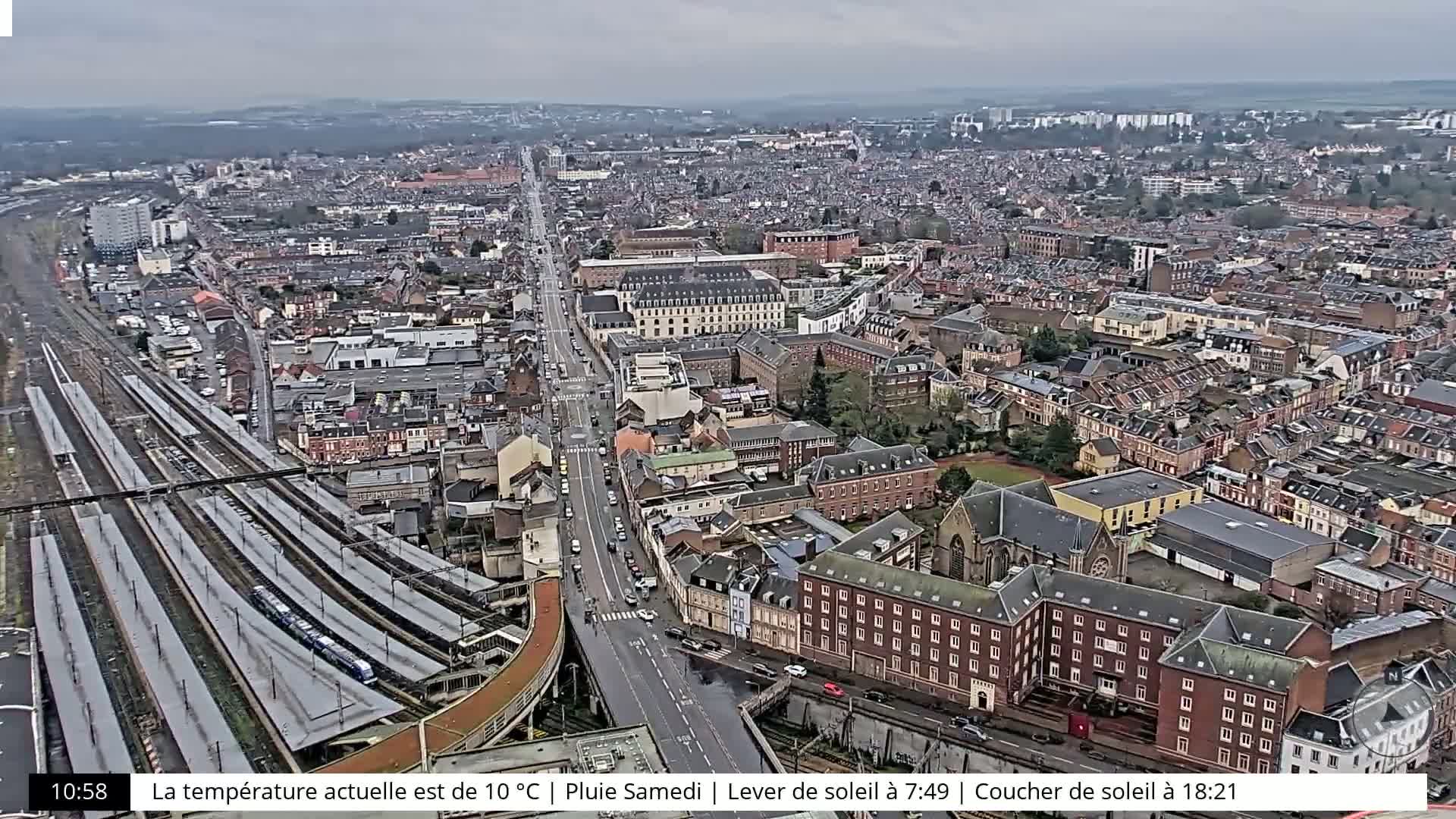 A high-angle view of a city on a rainy Saturday, showing a railway station, numerous buildings, and a long road.