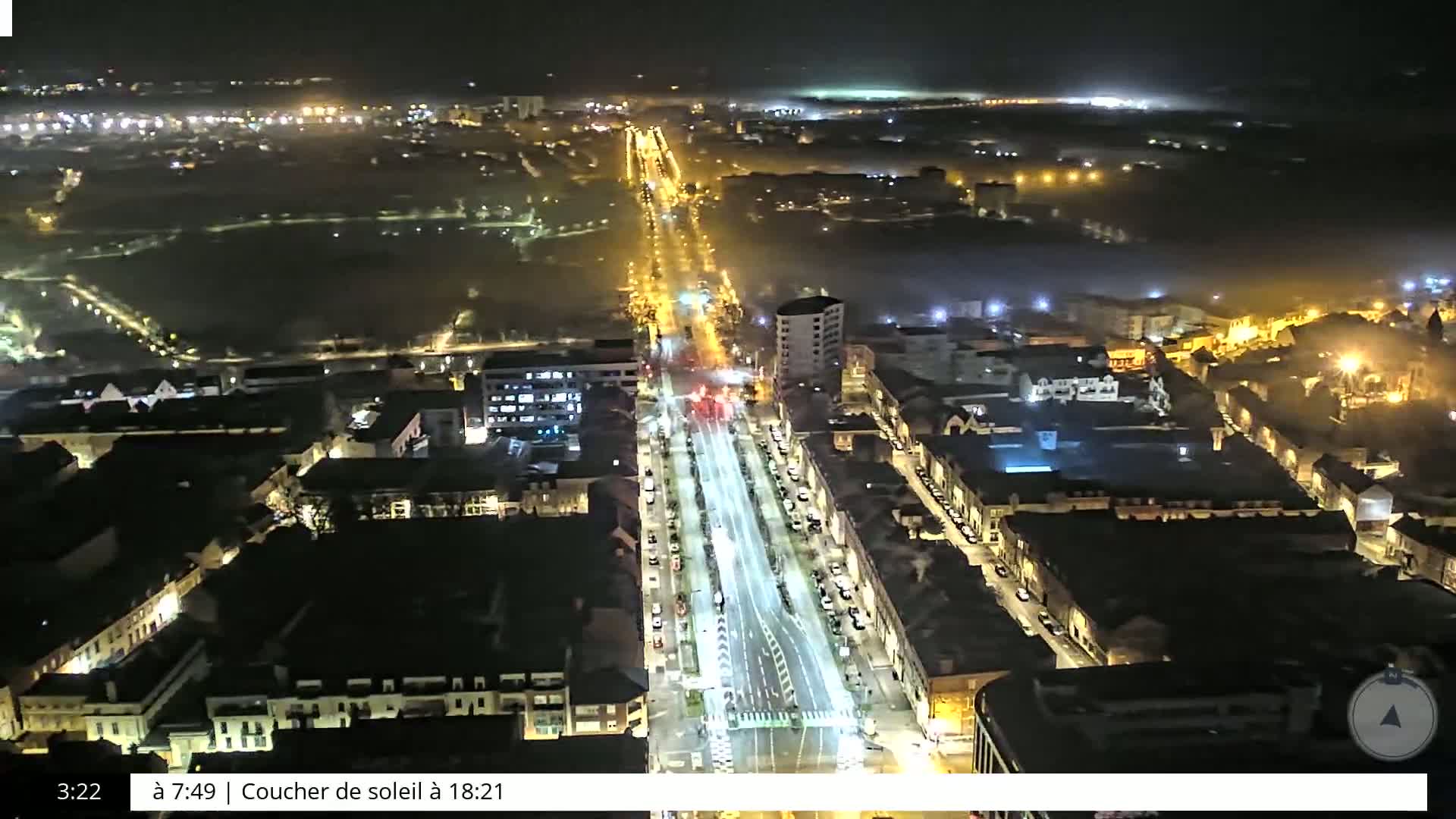 A nighttime aerial view of a city street illuminated by streetlights, with a foggy or hazy atmosphere.