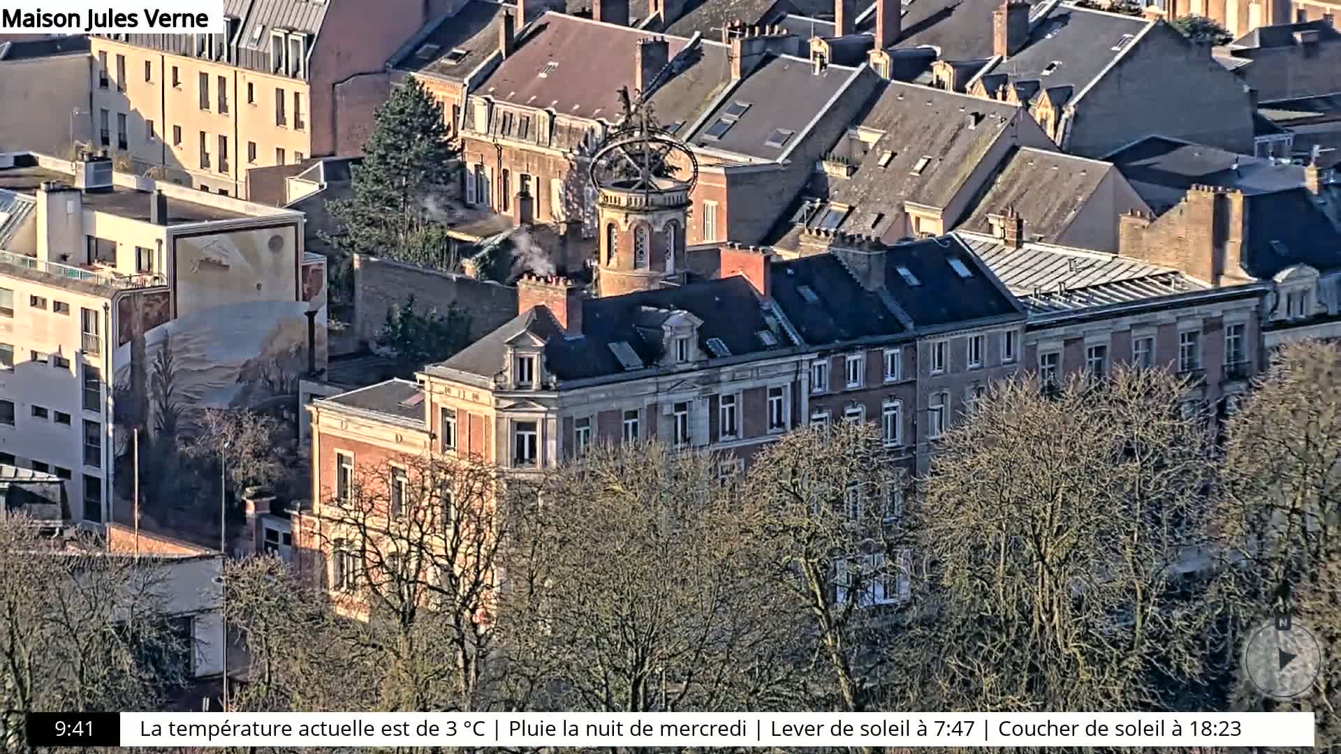 A high-angle view of a city block with many buildings, some with visible rooftop features, partially obscured by bare winter trees.