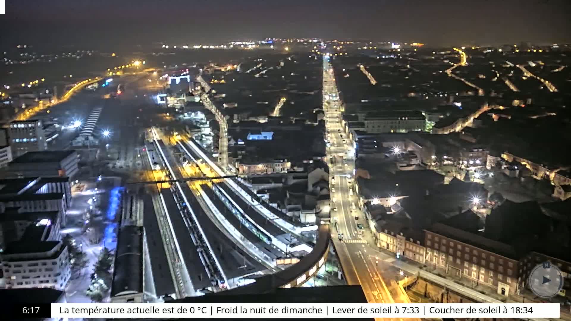 A nighttime aerial view of a city's train station and surrounding streets, illuminated by streetlights.