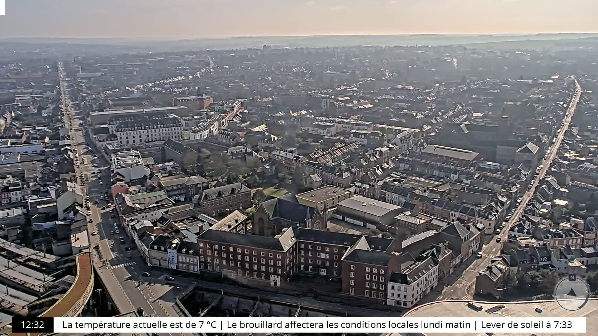 A hazy aerial view shows a dense city with a long, straight road cutting through it, extending to a body of water in the distance.
