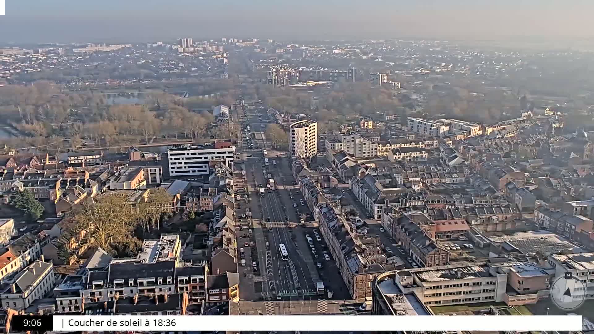 A high-angle, long shot of a city on a hazy day shows a wide street with traffic and numerous buildings stretching into the distance.