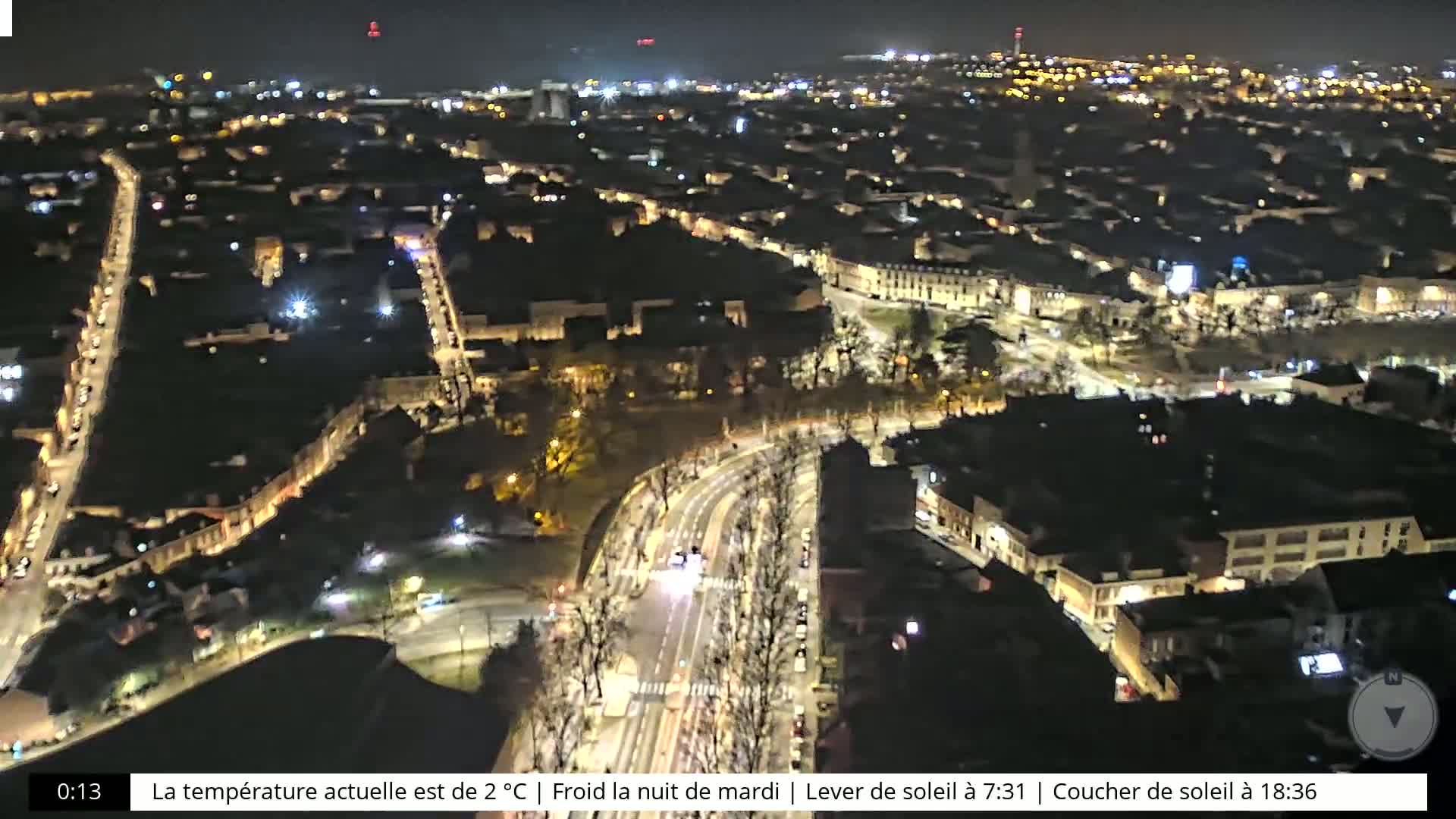 A nighttime aerial view of a city with illuminated streets and buildings under a cold, clear sky.