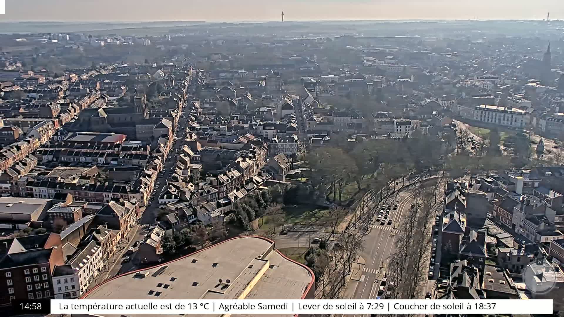 A sunny aerial view of a city with many buildings and streets, showing a mostly clear sky.