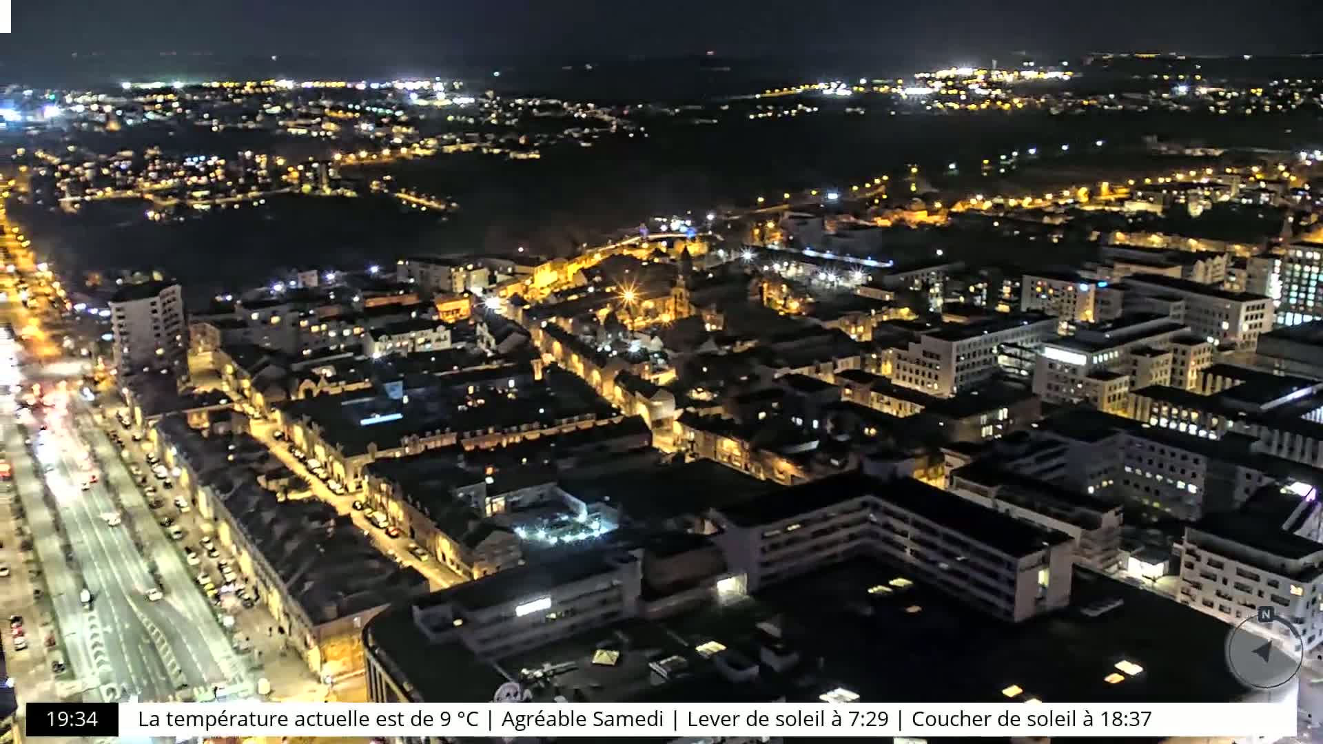 An aerial nighttime view of a city with brightly lit streets and buildings under a clear sky.
