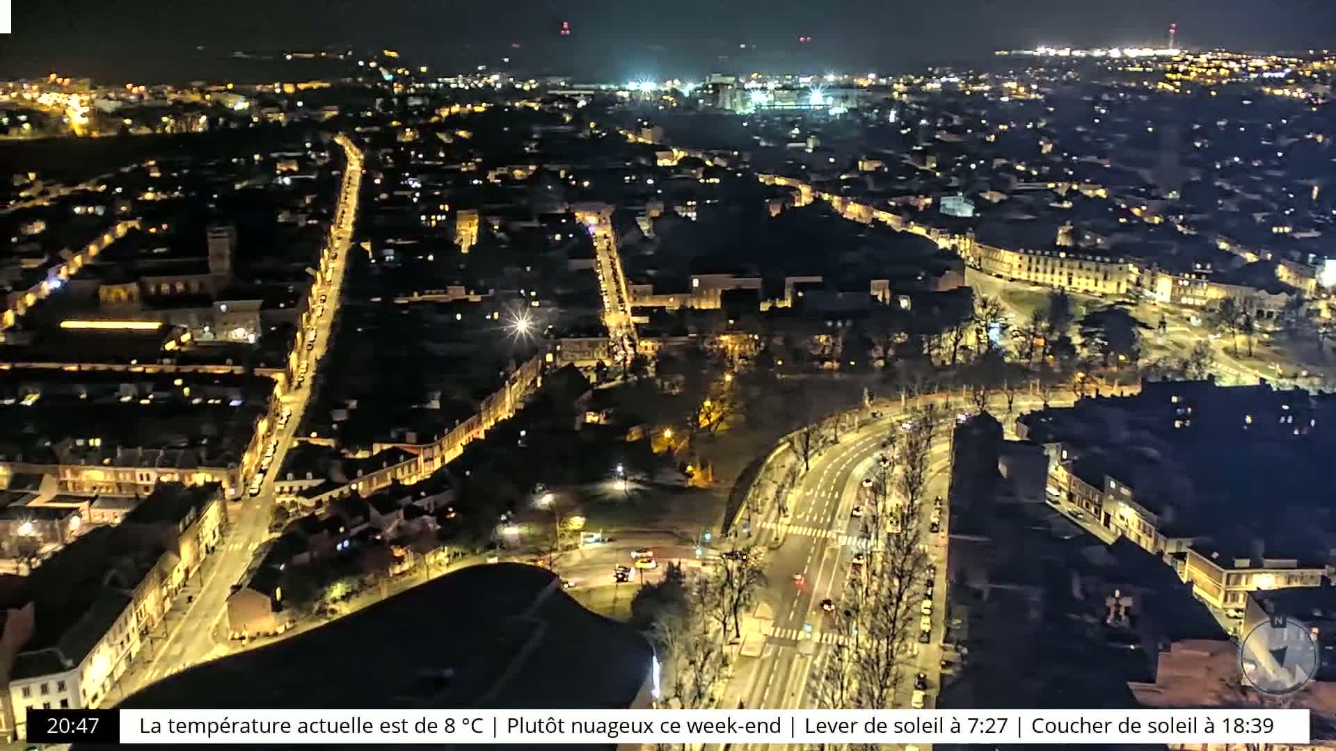 A nighttime aerial view of a city with illuminated streets and buildings under a mostly cloudy sky.