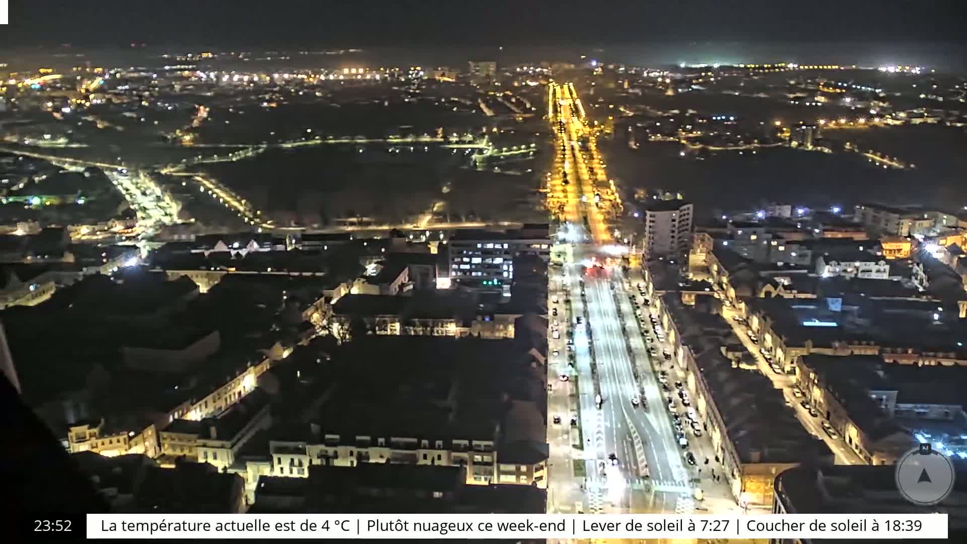 A nighttime aerial view shows a city with a long, brightly lit street running through it.